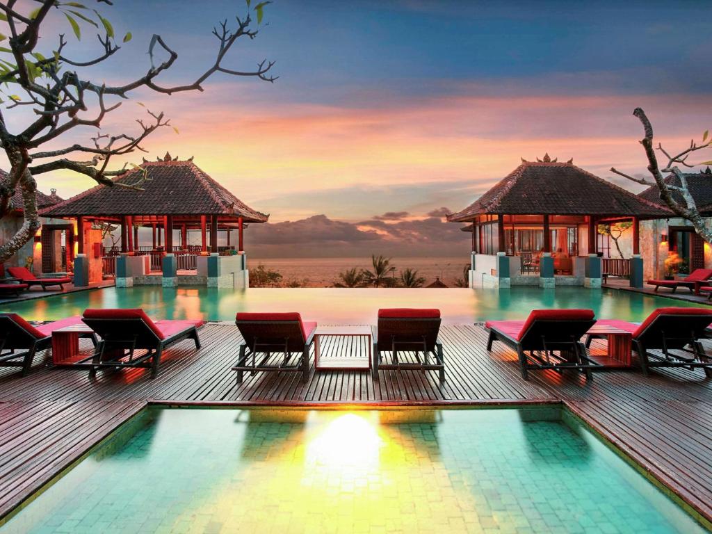 库塔巴厘岛库塔美居酒店的一个带游泳池和椅子的度假村,享有日落美景