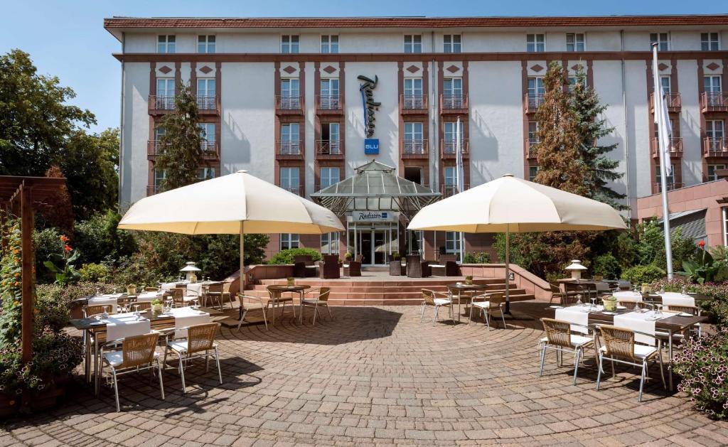 梅泽堡哈雷-梅森堡丽笙酒店的大楼前带桌子和遮阳伞的天井