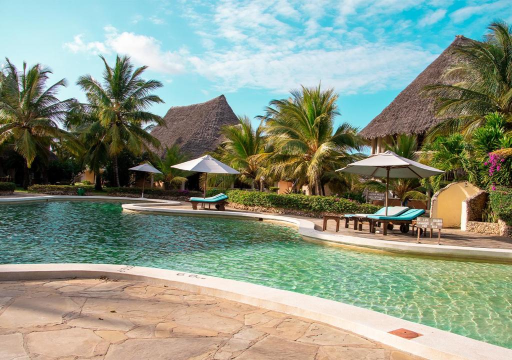 马林迪Tembo Court Apartments的一个带长椅和遮阳伞及棕榈树的度假游泳池