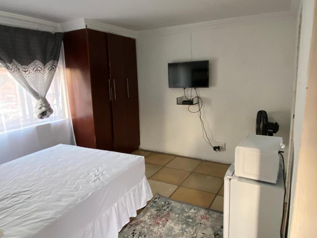索韦托Soweto Towers Guest Accommodation的一间卧室配有一张床、一台电视和一台冰箱