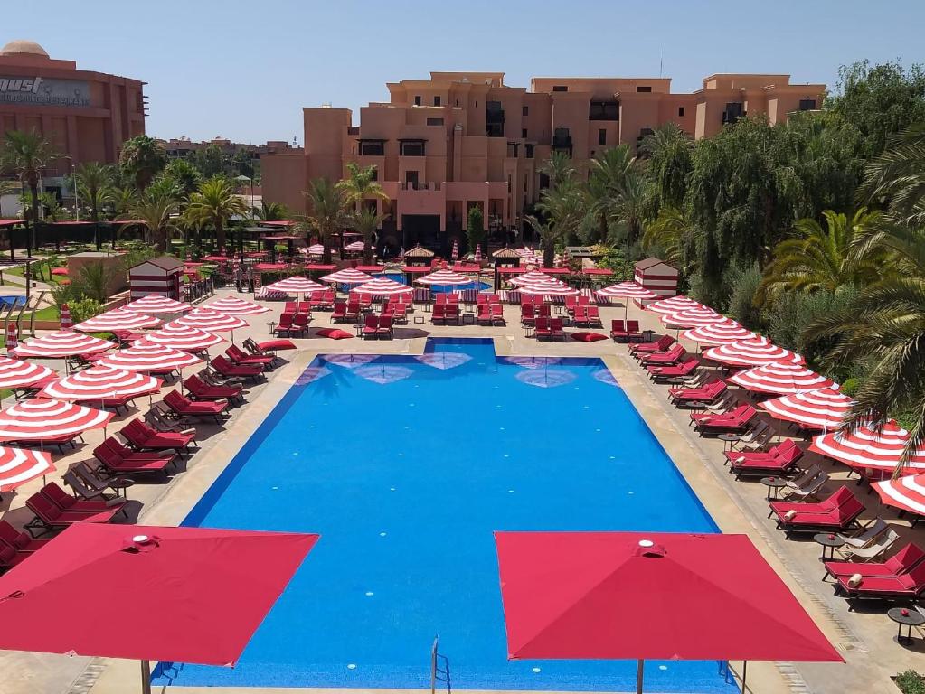 马拉喀什马拉喀什莫凡彼酒店的一个带红色和白色遮阳伞及椅子的度假游泳池