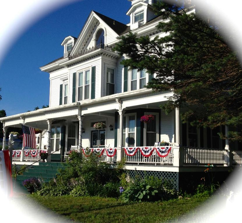 Center Harbor中心海港萨顿之家住宿加早餐旅馆的前廊上悬挂着美国国旗的白色房子