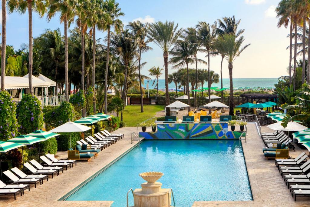 迈阿密海滩金普顿赛康贝酒店的度假村的游泳池配有躺椅和棕榈树