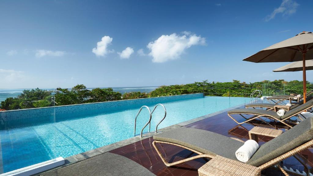 沙努尔Holiday Inn Bali Sanur, an IHG Hotel的一个带椅子和遮阳伞的游泳池