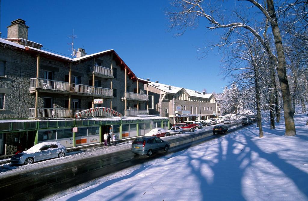 蒙卢伊Hotel et Résidence Le Clos Cerdan的一条雪覆盖的街道,在建筑物前停放汽车