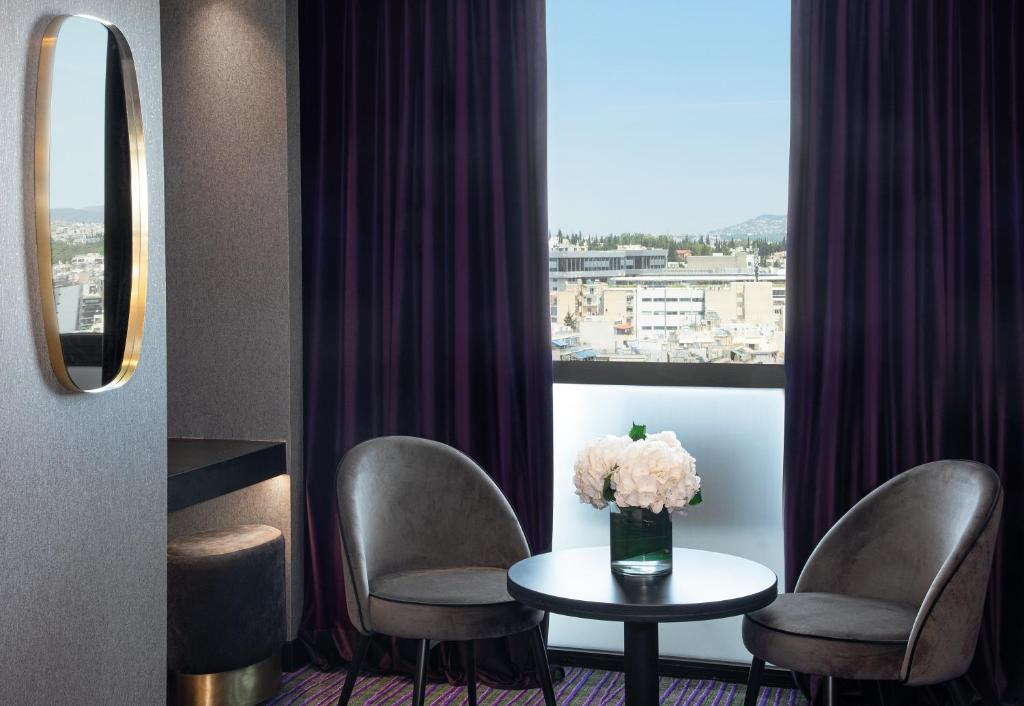雅典总统酒店的一间设有两把椅子、一张桌子和一个窗户的房间