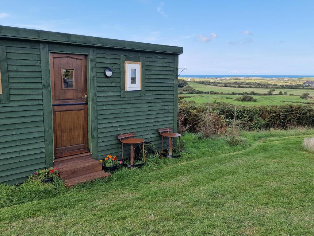 霍利黑德Stunning 1-Bed shepherd hut in Holyhead的绿色棚子,有两把长椅和一扇门