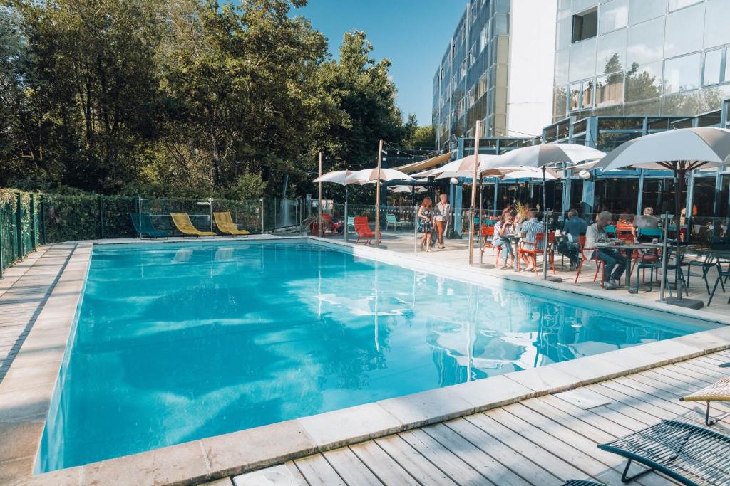 拉罗谢尔拉罗谢尔中心诺富特酒店的蓝色的游泳池,人们坐在桌子和遮阳伞下