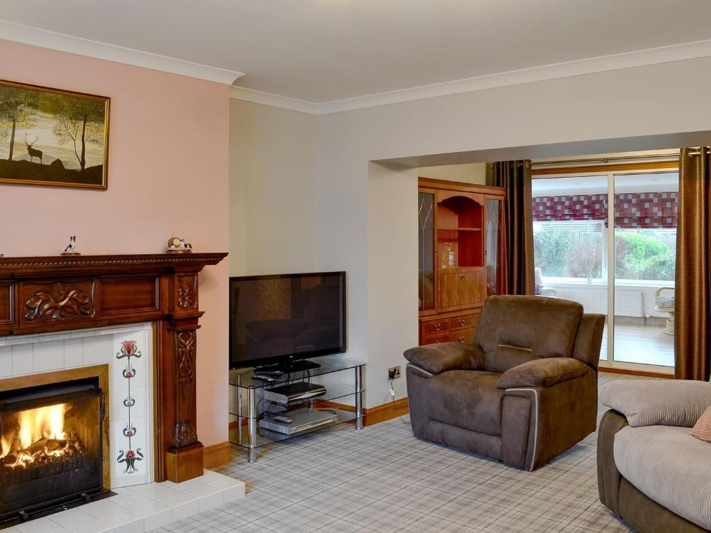 斯特兰拉尔Hawthorn Cottage的客厅设有壁炉、椅子和电视