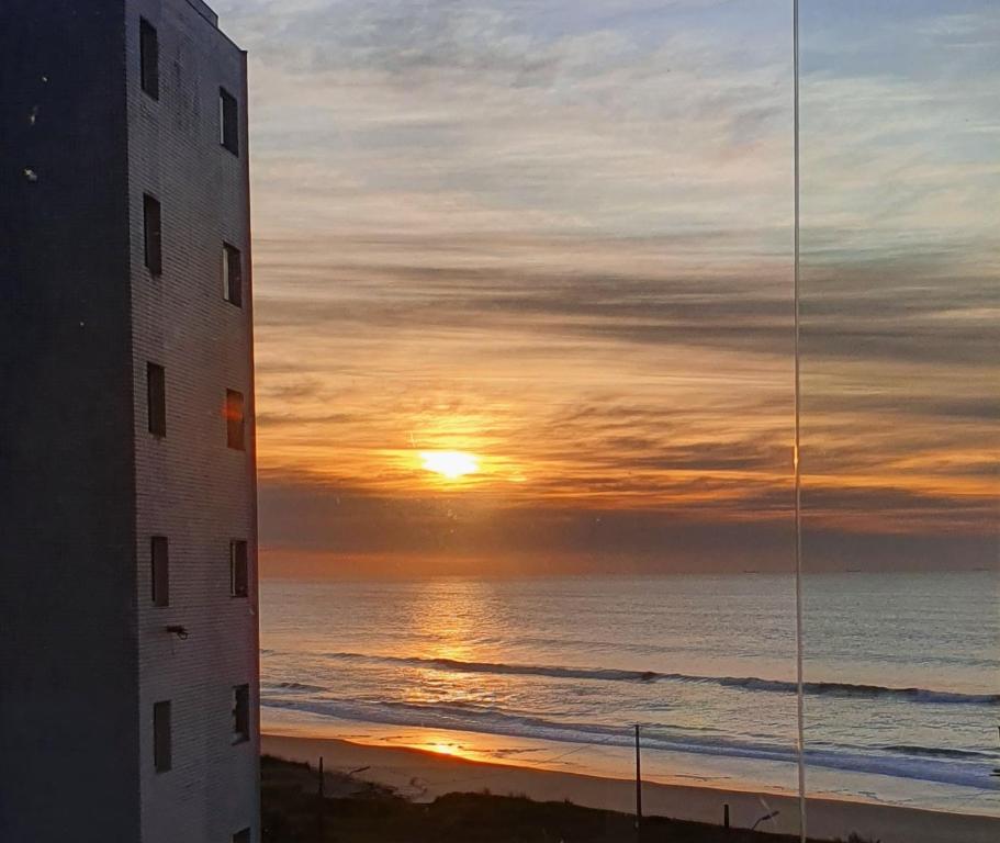 马蒂尼奥斯Apto Resort Cambuhy frente Mar até 6 pessoas的从两栋建筑之间的海滩上欣赏日落美景