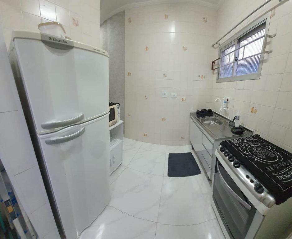 大普拉亚113 SOL & MAR I com VARANDA - 1 dormitório - Canto do FORTE - 300 m da Praia e 20m da Avenida dos Barzinhos - ESTACIONAMENTO gratuito e WI Fi 300mbytes com TV a cabo - ap113的白色的厨房配有炉灶和冰箱。