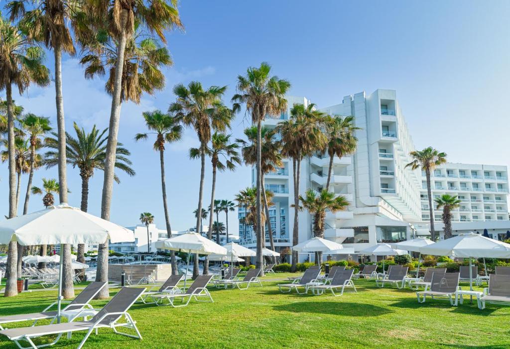 帕福斯莱昂纳多广场塞浦路斯马里斯海滩酒店及Spa的草坪,带椅子和棕榈树,建筑