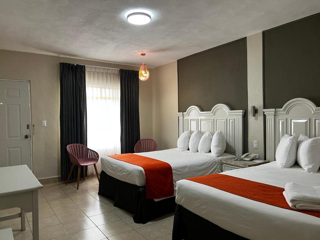 新拉雷多HOTEL LOS ROBLES的酒店客房带两张床和一张桌子以及椅子。