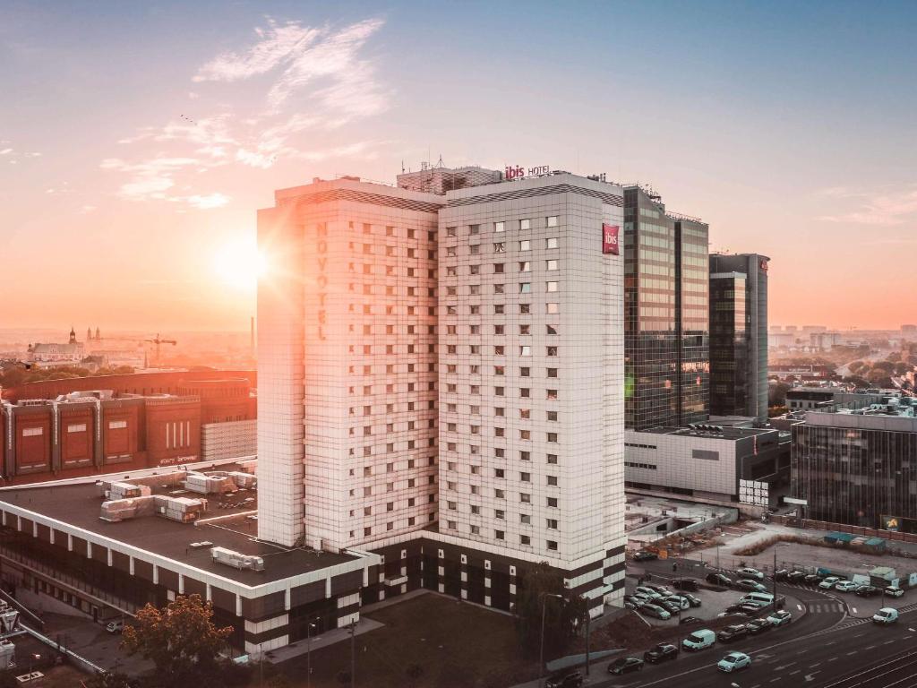 波兹南诺富特波兹南中心酒店的一座高大的白色建筑,太阳落在后面