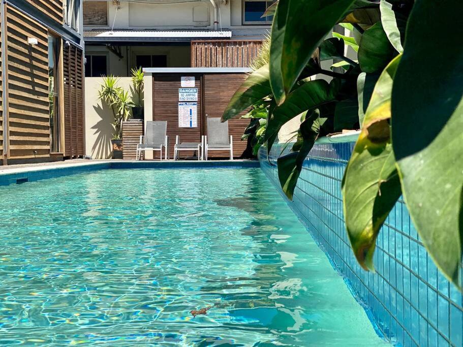 拜伦湾Poolside Apartment In Central Byron的拥有蓝色海水和绿色植物的游泳池