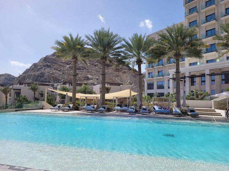 富查伊拉Address Beach Resort Residence Fujairah的棕榈树游泳池以及酒店