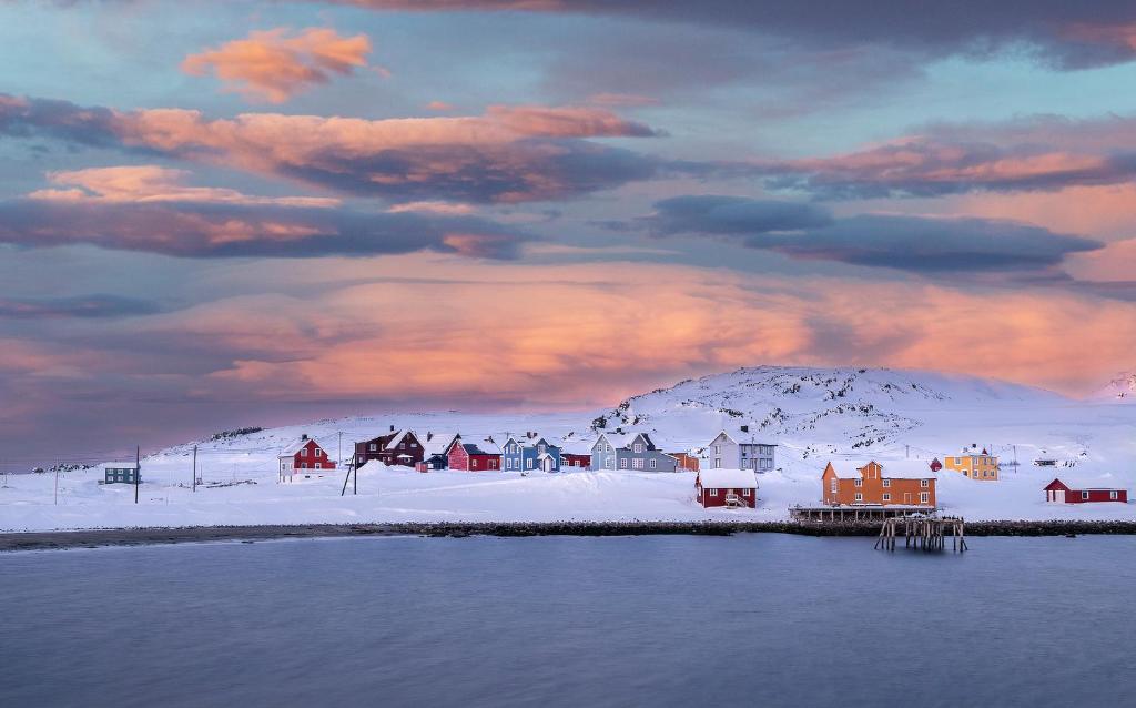 KongsfjordKongsfjord Arctic Lodge的白雪中的一个小镇,天空阴云