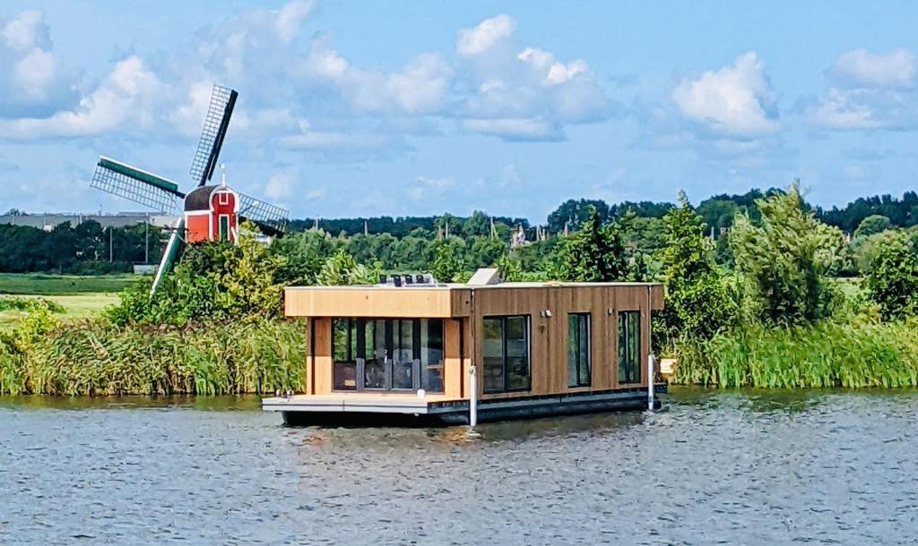 加赫Surla houseboat "Aqua Zen" Kagerplassen with tender的水面上的小房子,有风车