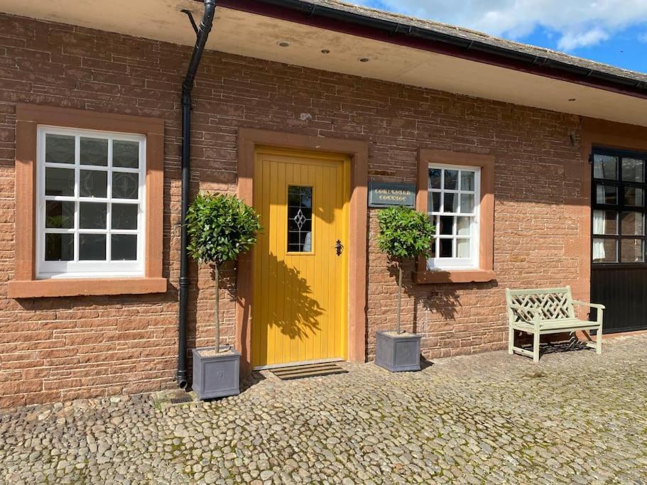 洛克比Courtyard Cottage的砖楼里一扇黄色的门,有长凳