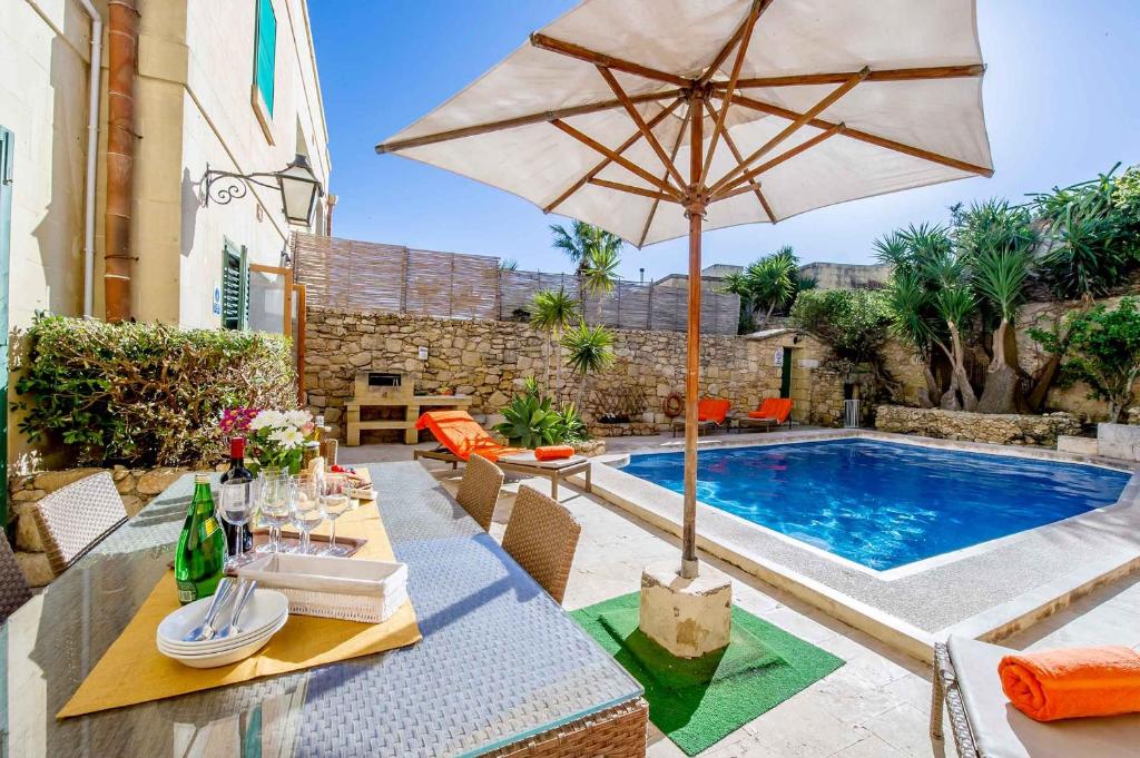 萨奈特Djar Ta Menzja 3 Holiday Home的庭院设有带遮阳伞的桌子和游泳池。
