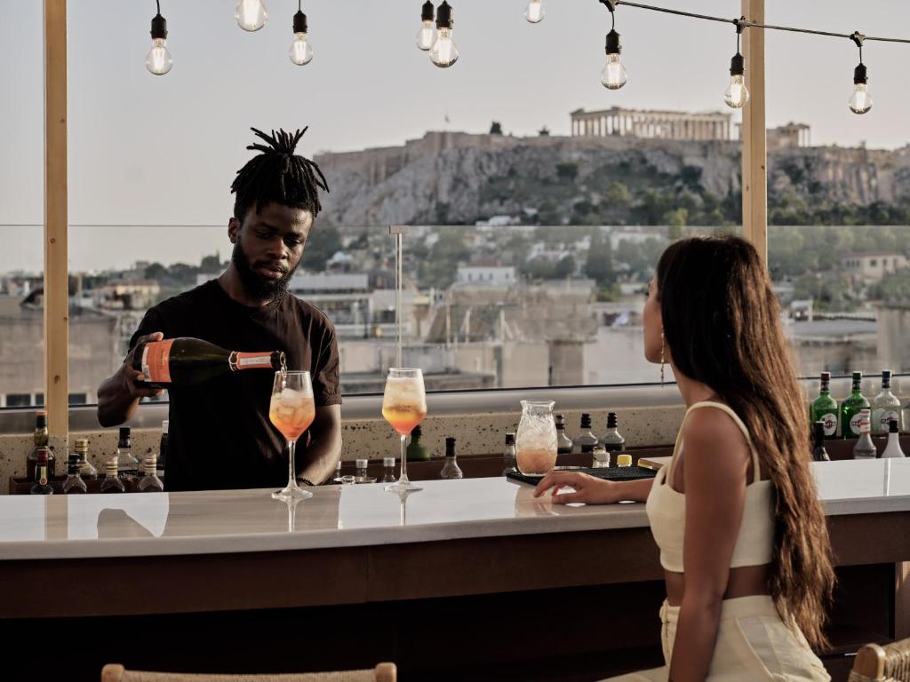 雅典The Lekka Hotel & Spa的男人在酒吧里把饮料倒给女人