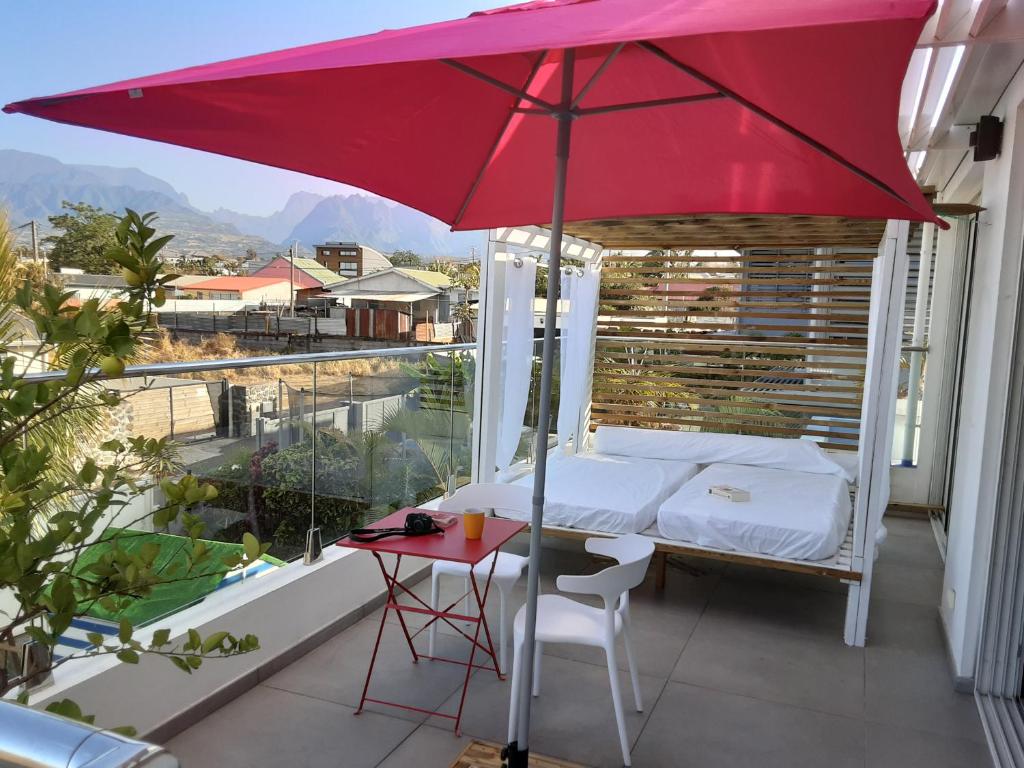 圣皮埃尔Maison TONGA piscine /jacuzzi chambre de luxe的阳台的红色遮阳伞,配有一张床和一张桌子
