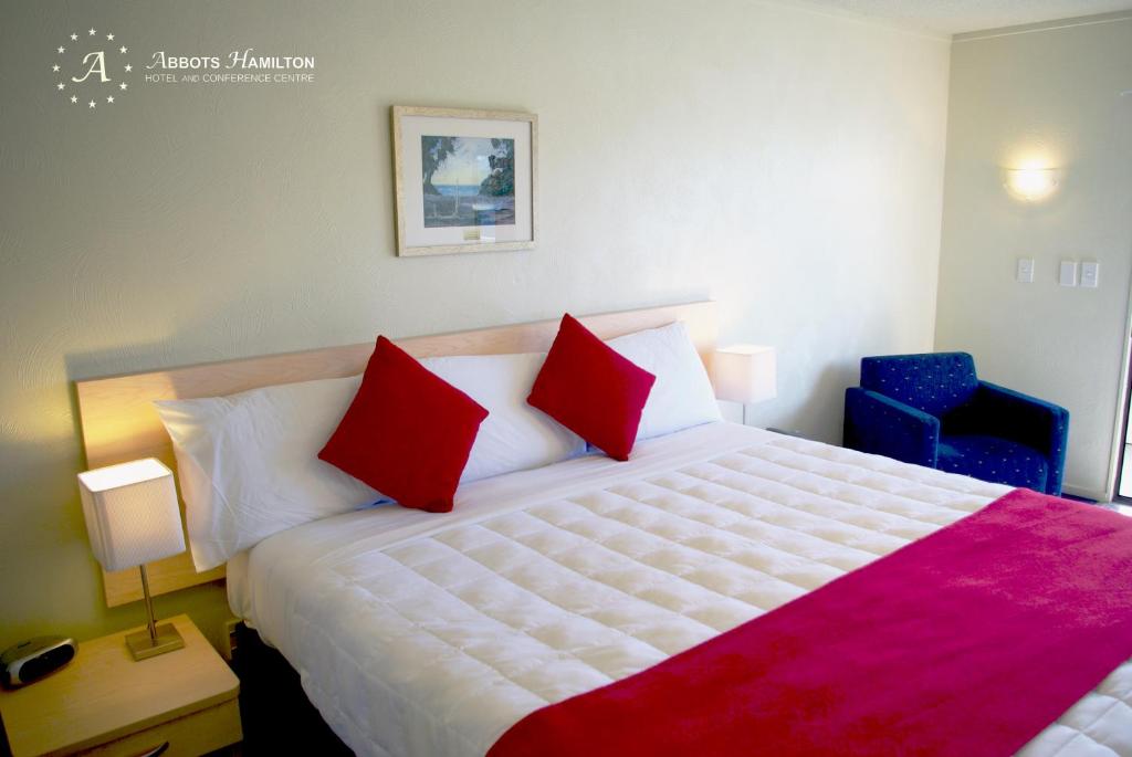 汉密尔顿阿博茨汉密尔顿 - 酒店及会议中心的一间卧室配有一张大床和两个红色枕头