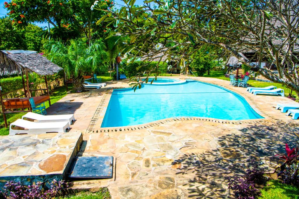 迪亚尼海滩Oasis Diani Beach Villas的庭院内的游泳池,带椅子和树木