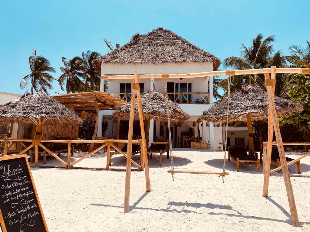 布韦朱Helwas Zanzibar Beach Hotel的海滩上带草伞和标志的度假胜地