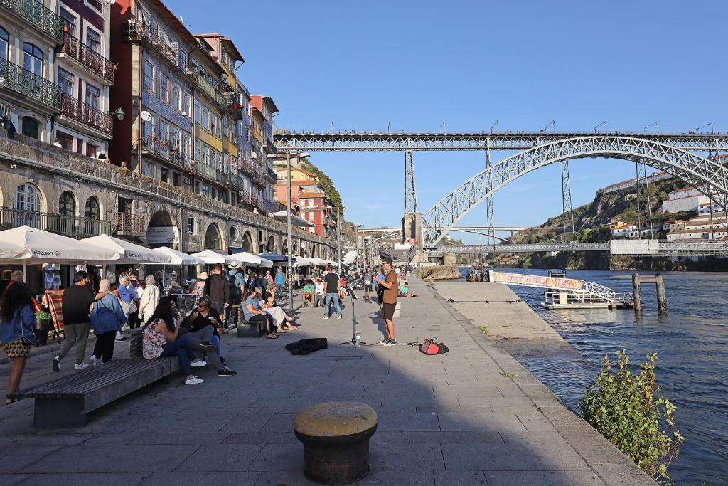 波尔图FLH Porto Ribeira with River View的一群人坐在水边的人行道上,有桥