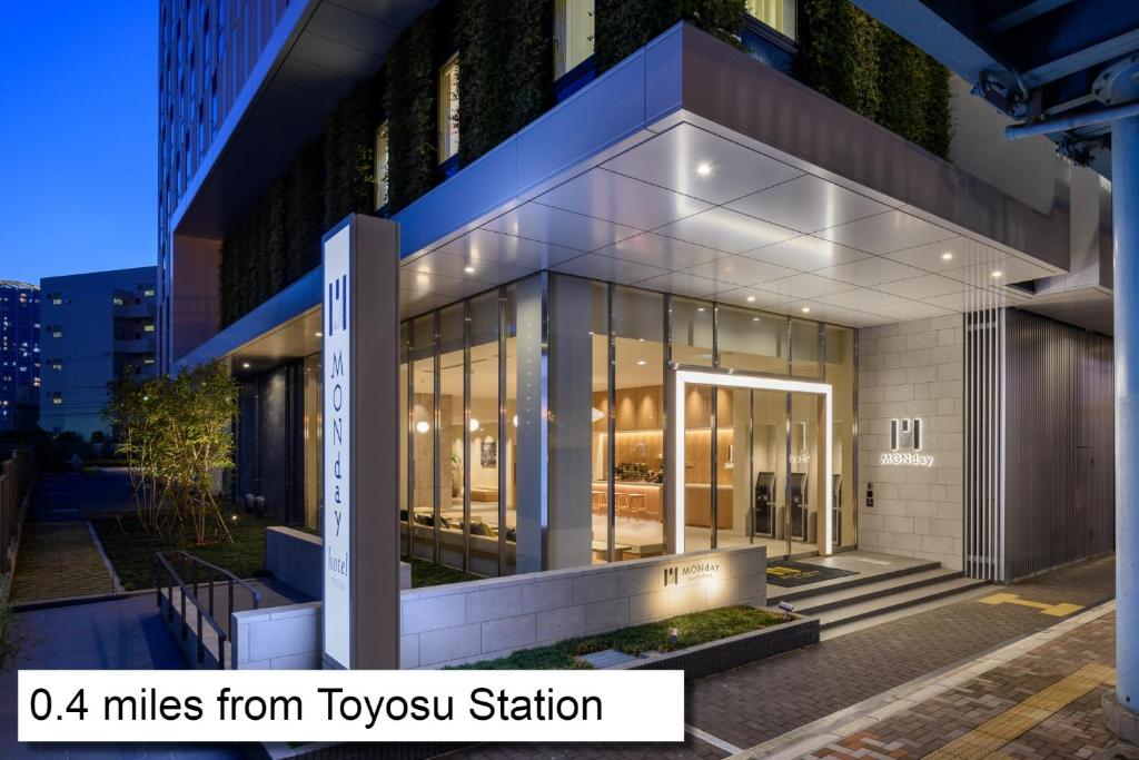 东京hotel MONday Premium TOYOSU的一座建筑,带有玻璃窗和标志,距离泰森车站有几英里远