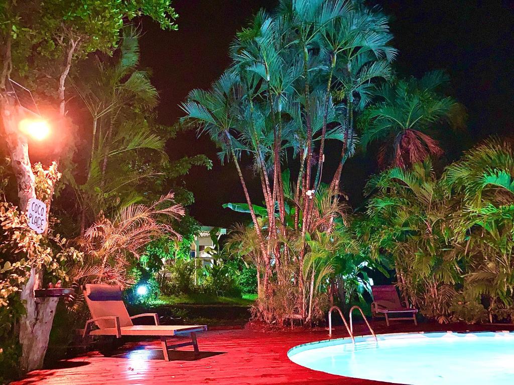 勒卡尔贝LODGE PAMPLEMOUSSE avec PISCINE privative , dans parc calme à 500 m plage的游泳池在晚上设有椅子和棕榈树