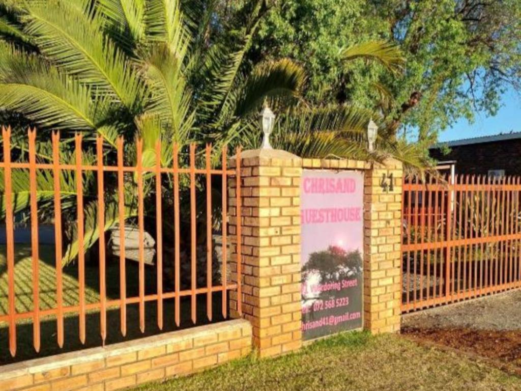 库鲁曼Chrisand Guesthouse的棕榈树前有标志的栅栏