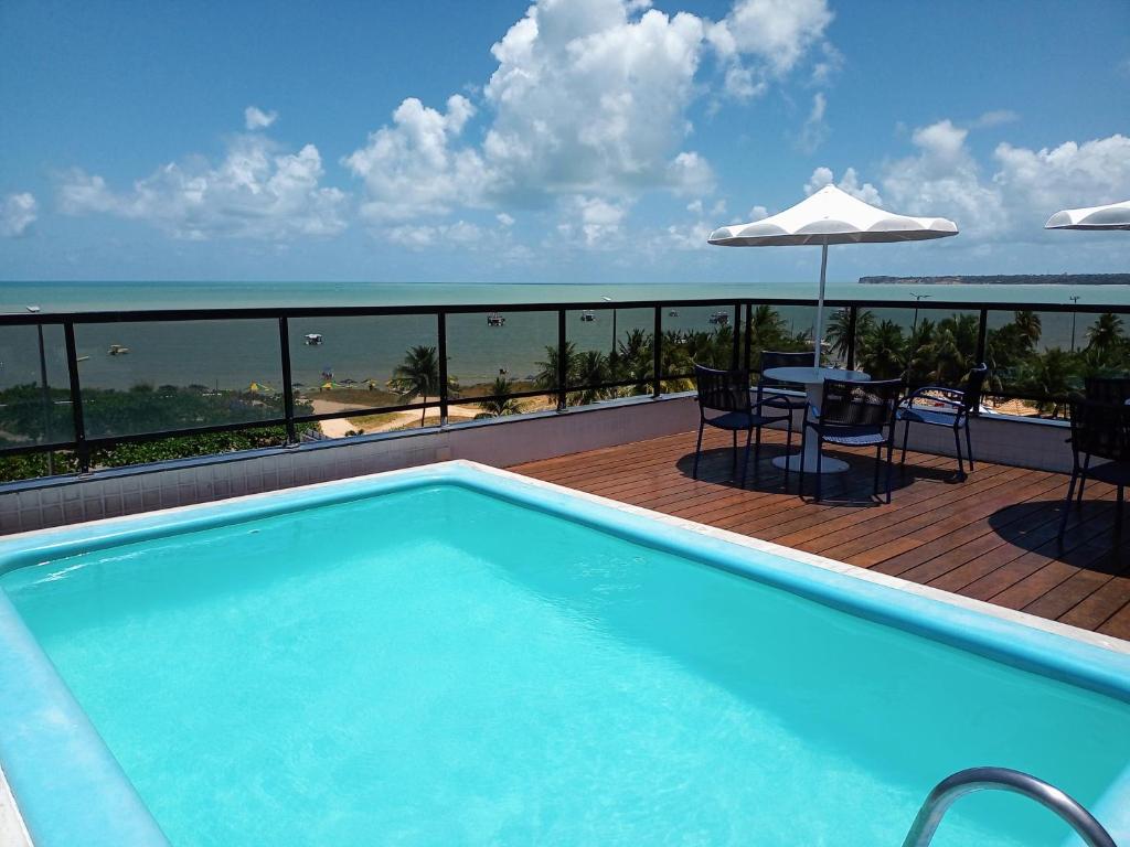 若昂佩索阿Flat pé na areia Tambaú的阳台的游泳池配有桌子和遮阳伞