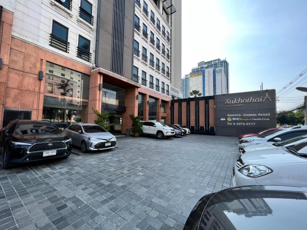 曼谷Sukhothai Hotel and Residence的停车场,停车场的汽车停在大楼前