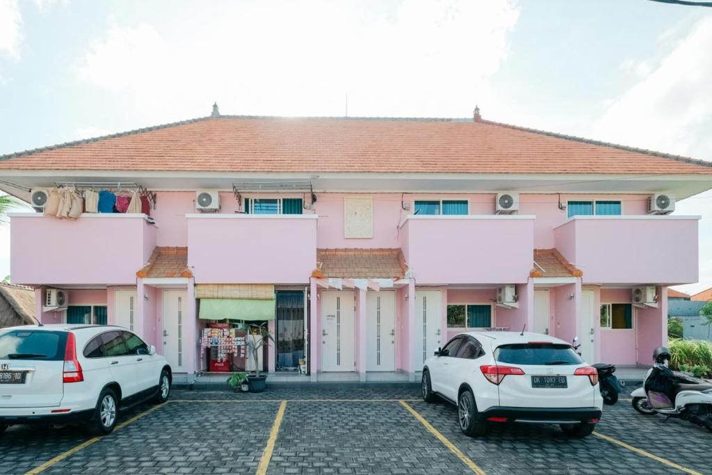 BalianRedDoorz at Kawaii Apartment Jimbaran的两辆汽车停在一个粉红色建筑前面的停车场