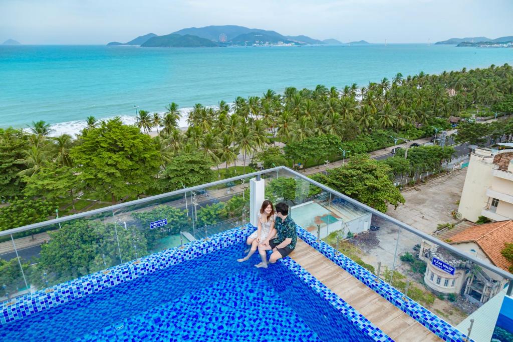 芽庄Azura Gold Hotel & Apartment的一对夫妇坐在游泳池边,俯瞰大海