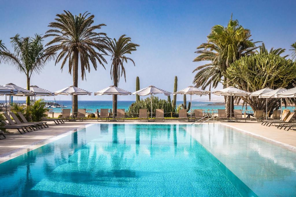 卡勒达德福斯特Barceló Fuerteventura Royal Level - Adults Only的一座棕榈树和遮阳伞的游泳池