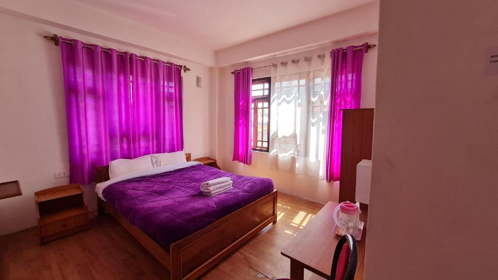 PemayangtseHotel Himsagar的一间卧室配有粉红色窗帘和一张紫色床单