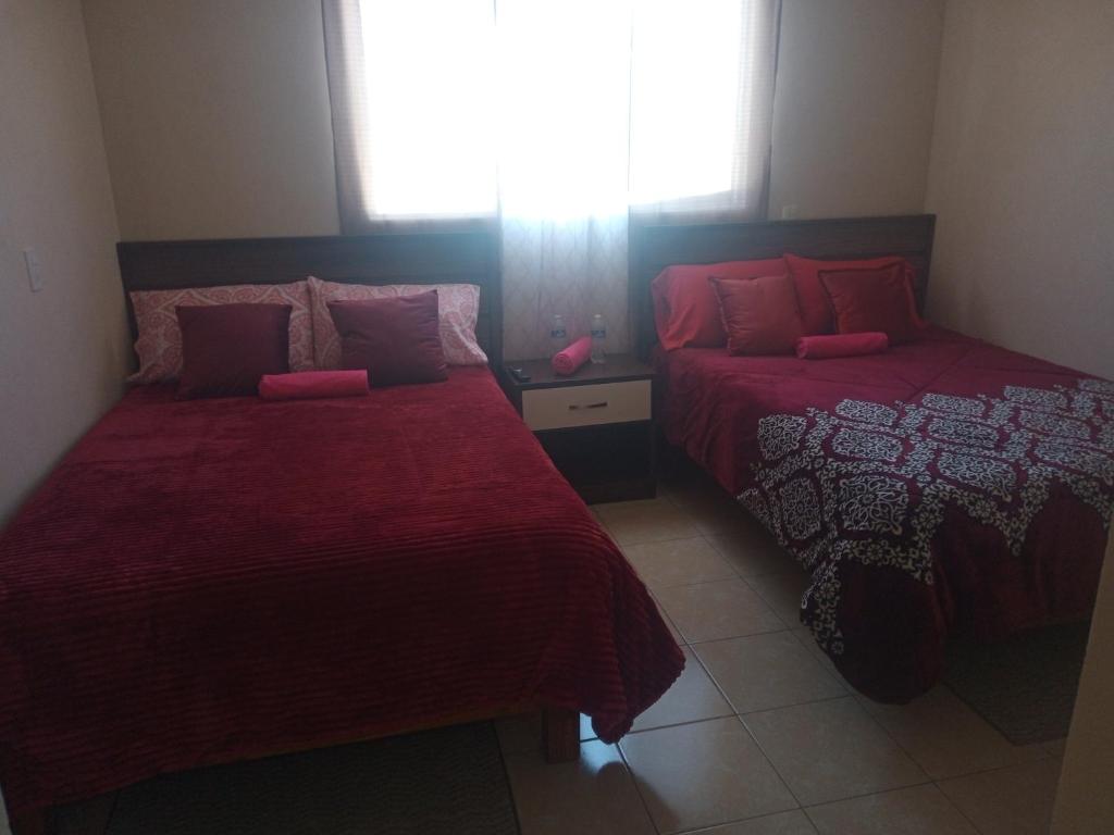 萨卡特兰La casa de las flores的一间卧室设有两张带红色床单的床和窗户。