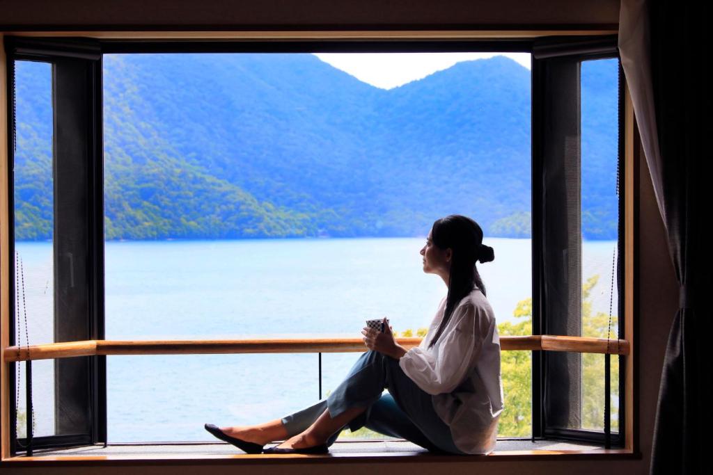 日光Yutorelo Nikko的坐在窗台上看着湖面的女人
