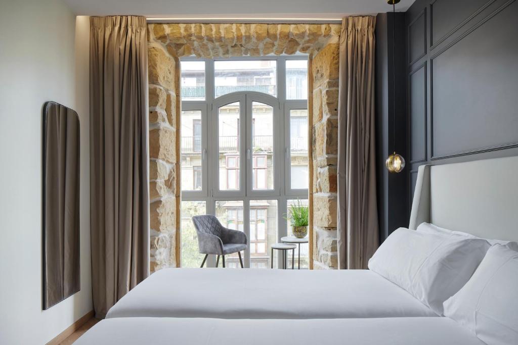 圣塞瓦斯蒂安HOTEL ARRIZUL CATEDRAL的一间卧室配有一张床和一个带椅子的窗户