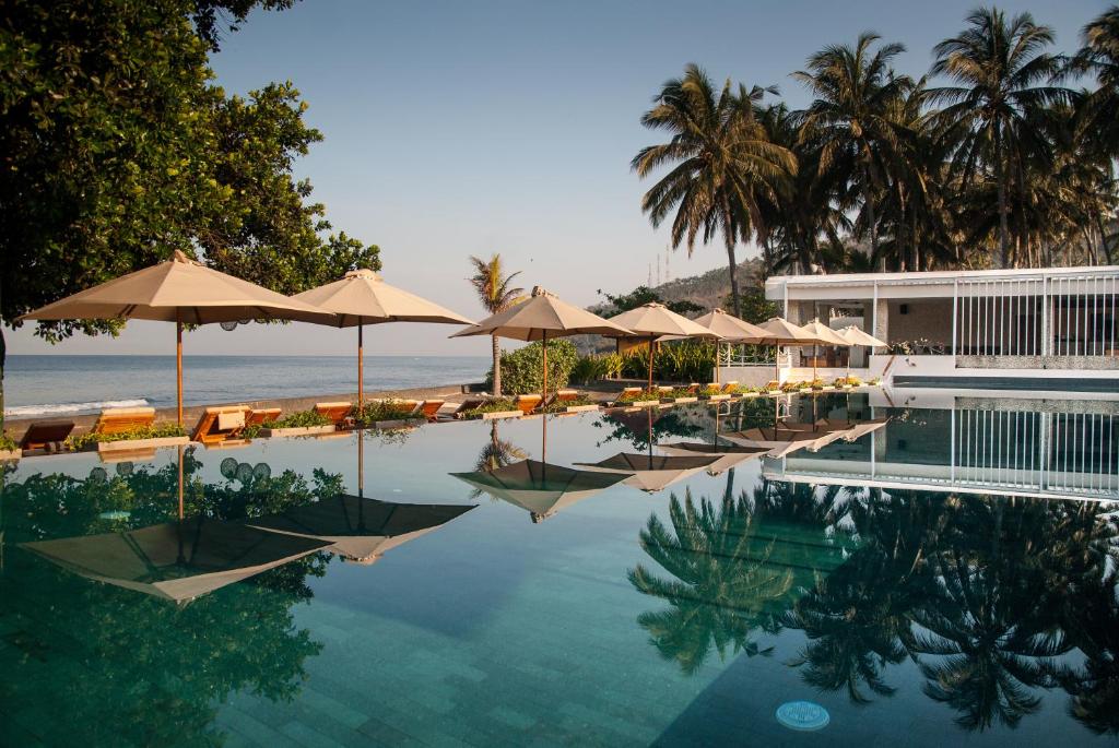 圣吉吉生活亚洲度假酒店的一个带遮阳伞和椅子的游泳池以及大海