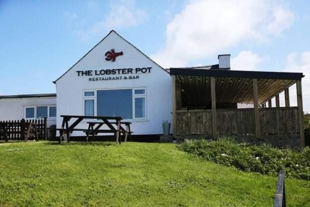 LlanrhyddladThe Lobster Pot Cottage Church Bay的前面有一张野餐桌的建筑