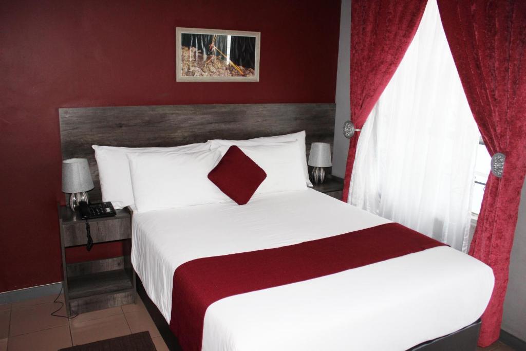 哈博罗内Platinum Hotel的卧室配有一张带红色窗帘的大型白色床