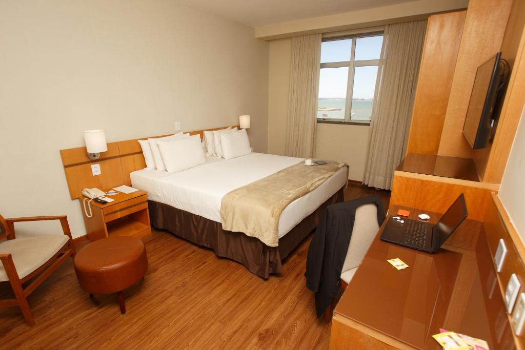 维多利亚Vitoria Praia Hotel的酒店客房配有一张床、一张书桌和一台笔记本电脑