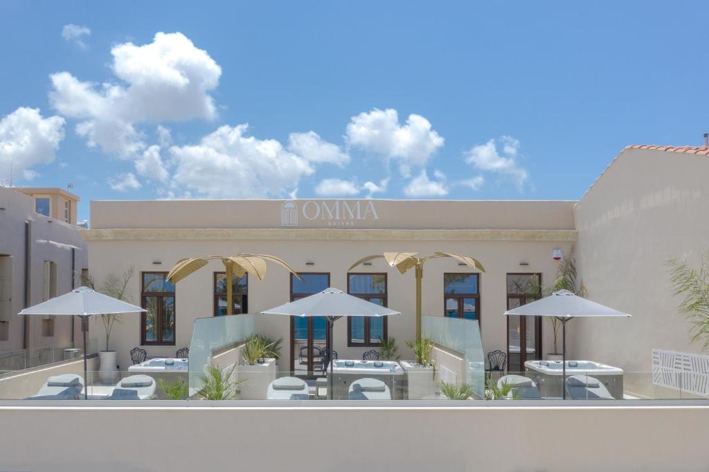 罗希姆诺Omma Suites的一张带有桌子和遮阳伞的酒店前部的 ⁇ 染