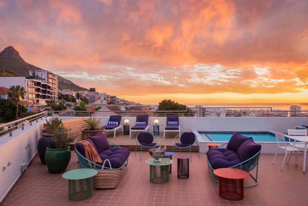 开普敦Home Suite Hotels Sea Point的屋顶甲板配有桌椅,享有日落美景