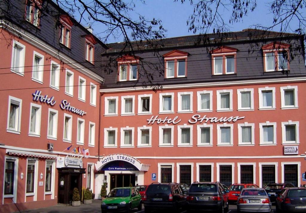 维尔茨堡施特劳斯城市伙伴酒店的一座大型红色建筑,前面有汽车停放