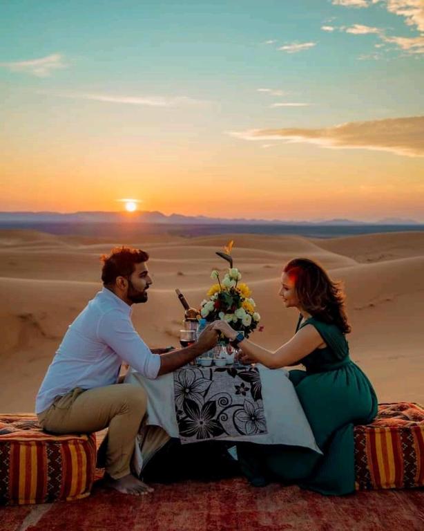 伊尔富德sahara luxury desert camp的坐在沙漠桌子上的男人和女人